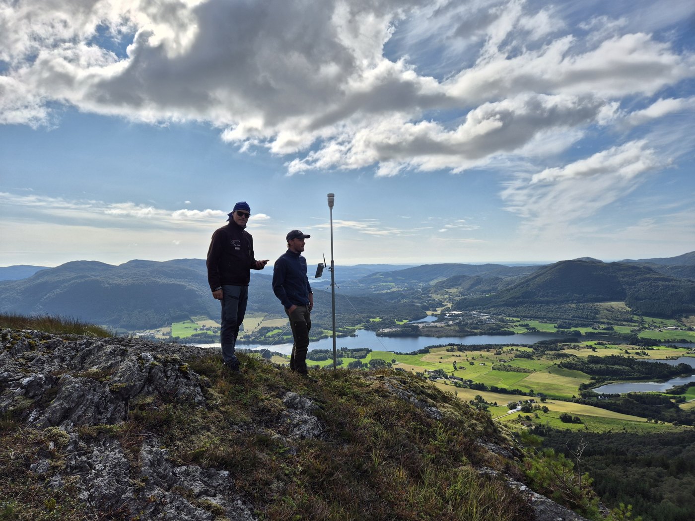 Two people beside a Bakvind weather station on a mountain.